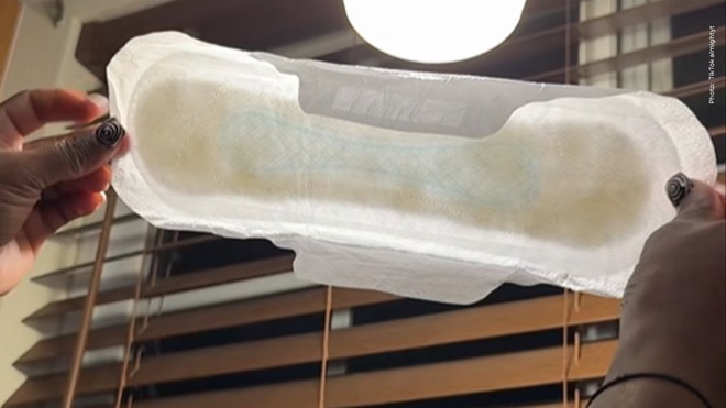 femme tenant une serviette hygiénique avec taches noires dans les mains