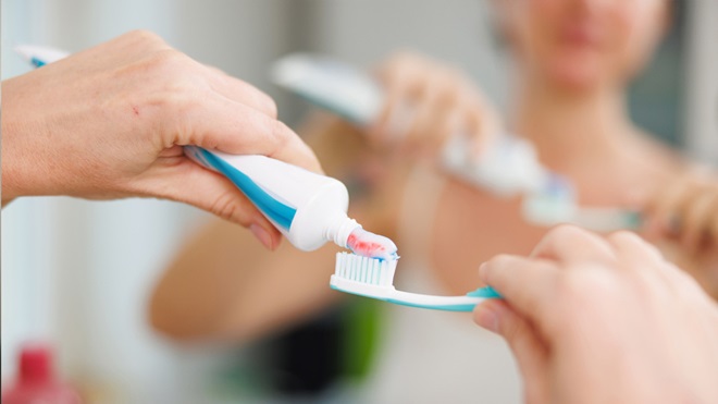 femme qui dépose du dentifrice sur une brosse à dents devant un miroir 