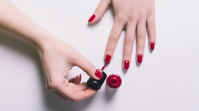 femme qui met du vernis à ongle rouge