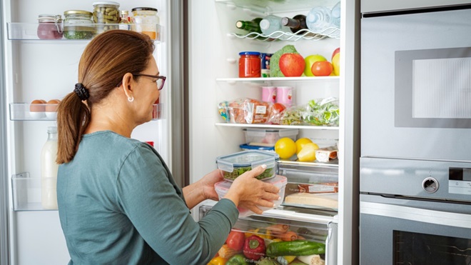 Une femme range ses courses dans son frigo