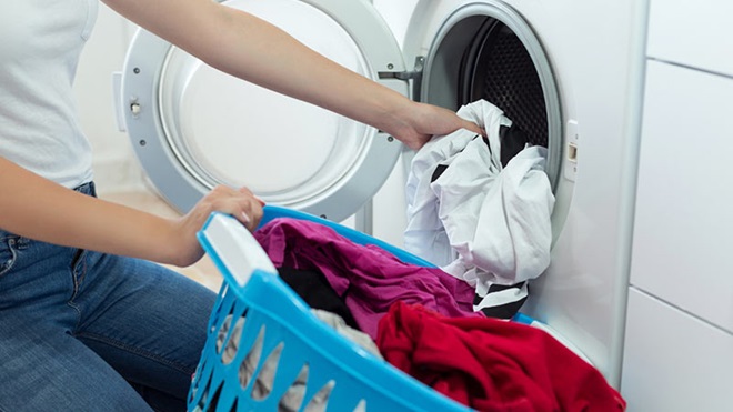 Femme qui mets du linge dans la machine a laver