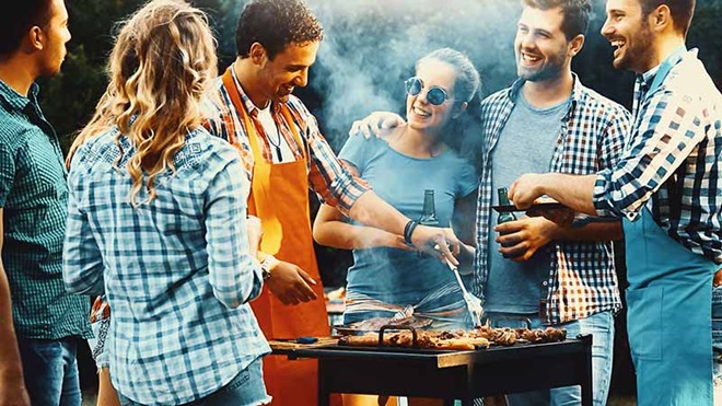groupe d'amis devant un barbecue au gaz ou charbon