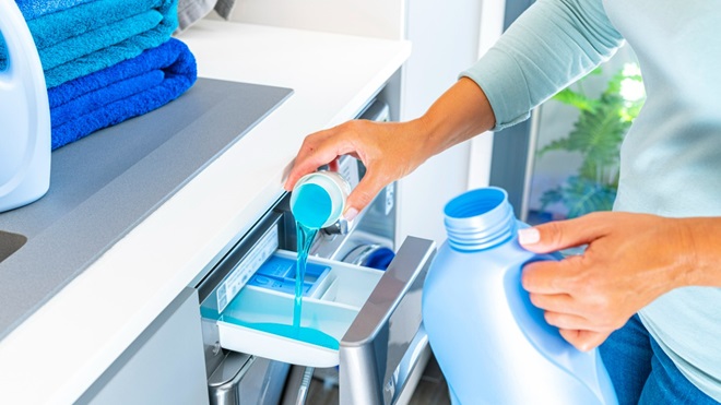 main mettant une dose de lessive dans une machine à laver pleine