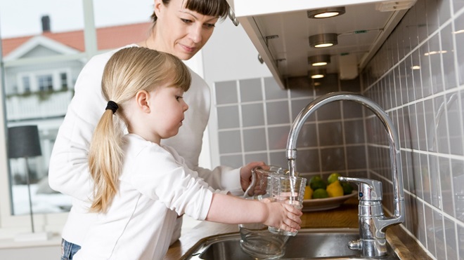 Une petite fille se servant un verre d'eau au robinet de la cuisine.